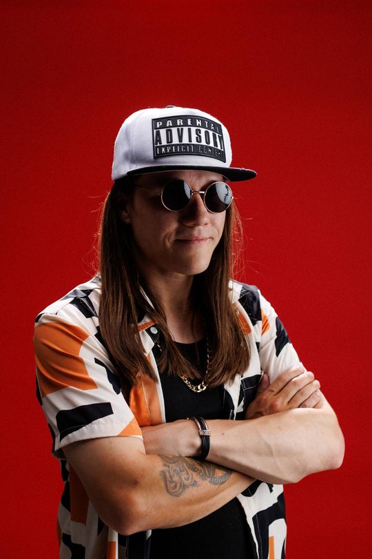 Mon'et, arms crossed, red backdrop.